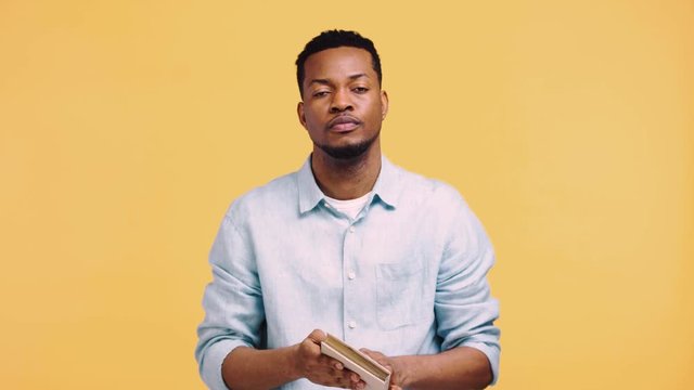 bored african american man holding book above head isolated on yellow