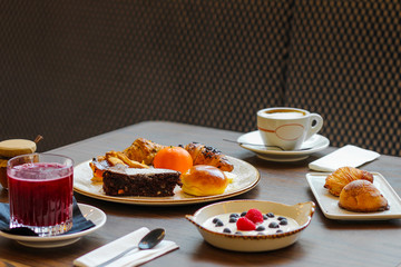 breakfast table with chocolate cakes, jam, red orange juice, mandarin, croissants, butter, cappuccino, sfogliatella, yogurt with raspberries and blueberries - 309275342