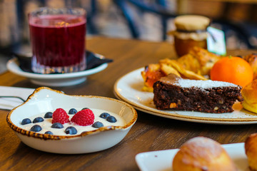 detail of breakfast table with chocolate cakes, jam, red orange juice, mandarin, croissants, butter, yogurt with raspberries and blueberries - 309275345
