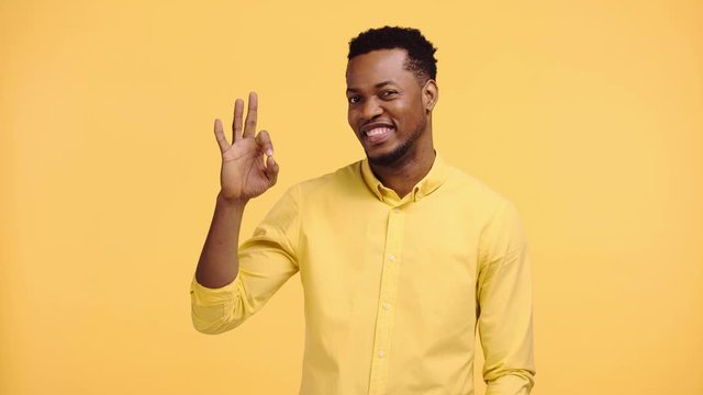 smiling african american man showing okay sign isolated on yellow
