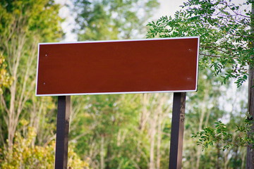 Blank brownish red sign in a park with trees surrounding background