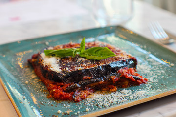 close up shot of eggplant parmigiana with parmesan cheese, fresh basil and tomato in Italian restaurant