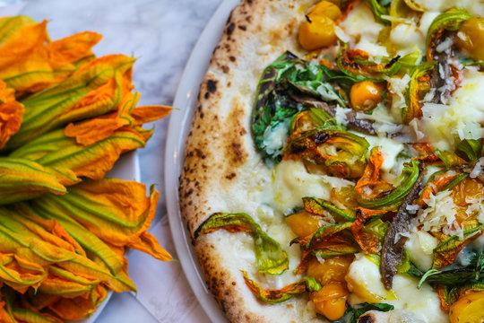 top view of pizza with zucchini flowers, fresh mozzarella cetara anchovies, parmesan cheese and yellow tomatoes of Vesuvius