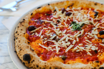 pizza maker is preparing a Gourmet pizza with San Marzano tomato sauce, black olives, capers, fresh basil, EVO oil and a sprinkling of pecorino in an Italian pizzeria