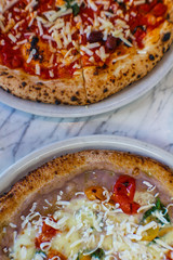 top view of two gormet pizzas on marble table of Italian pizzeria