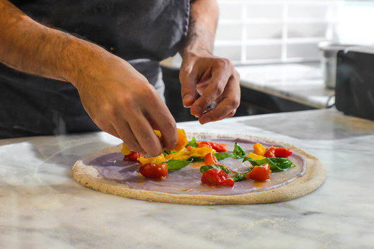 preparation of Pizza Bio in a traditional Italian pizzeria, prepared with wholemeal dough left to rest for at least 48 hours. On a base of purple potato velvety, there are red and yellow Piennolo cher