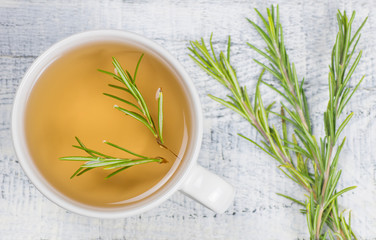 Top view white cup of healthy rosemary tea with fresh rosemary bunch on rustic background, winter herbal hot drink concept, salvia rosmarinus