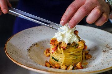 chef's hands plating a dish with spaghetti with lobster and buffalo stracciatella. In a luxurious Italian restaurant - 309278529