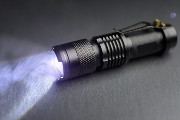 Fototapeta na wymiar Tactical waterproof flashlight. LED flashlight shines on the table in smoke.