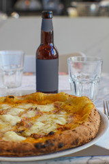 pizzeria table with craft beer with empty label and pumpkin cream pizza, bacon, grated provola and grana cheese and a drizzle of extra virgin olive oil.
