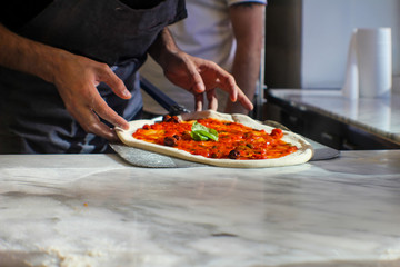 pizza maker is preparing a Gourmet pizza with San Marzano tomato sauce, black olives, capers, fresh basil, EVO oil and a sprinkling of pecorino in an Italian pizzeria