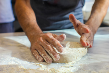 hands of pizza maker knead the dough for pizza with flour on a marble top of an Italian pizzeria