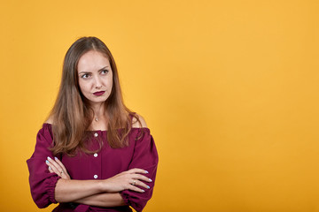 Obraz premium Ginger girl in burgundy bluse with bow over isolated orange background thoughtfully looks right folding her arms