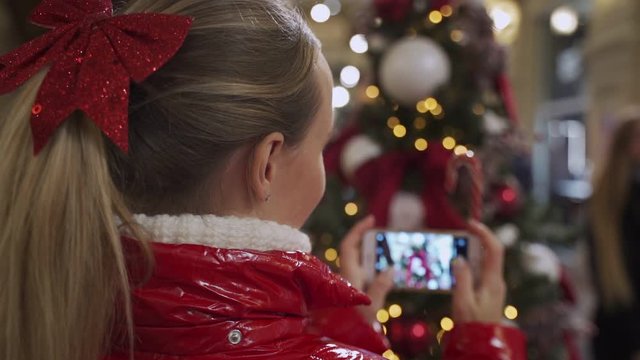 Woman photographing on smartphone christmas tree.