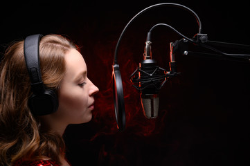 Vocalist, celebrity sings in a studio microphone with headphones on her head, live performance,...
