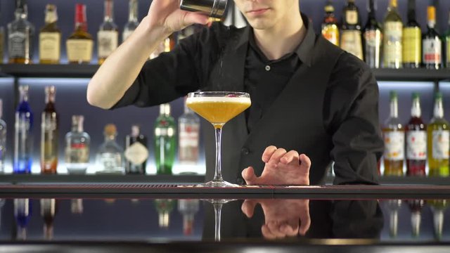 Bartender making cocktail into glasses on bar counter at night club. Blurred background. Preparing yellow alcoholic drink on bar