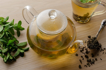 Cup and teapot of herbal tea with fresh mint on wooden boards
