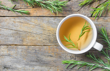 Top view white cup of healthy rosemary tea with fresh rosemary bunch on rustic background, winter...