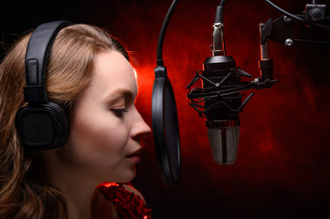 Girl sings in a red dress and red backlight. Microphone in a recording studio. Effective background. Vocal. Vocal schools and training.