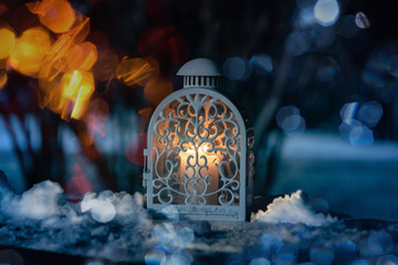A Christmas winter woodland snowing scene with a warm glowing lamp on a wooden table at night.