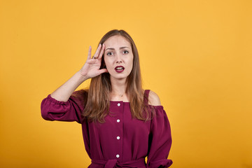 Girl over orange wall has just realized something and has intending the solution holding hand near head. Her blouse is burgundy.