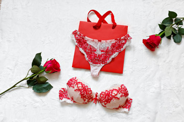 Women's erotic underwear and red roses on white surface. Red sexy lacy lingerie on white background. Concept of love. Flat lay. Copy space. Gift of a man - a woman on March 8 and Valentine's Day