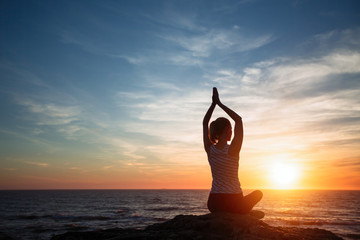 Yoga silhouette young woman on the sea coast at amazing sunset.