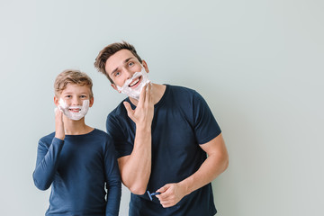Father with son applying shaving foam onto their faces against grey background
