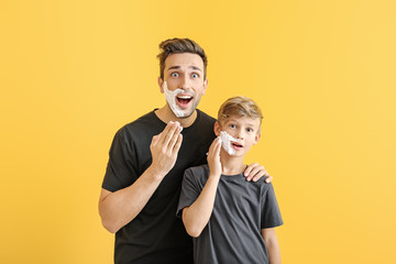 Funny father with son applying shaving foam onto their faces against color background