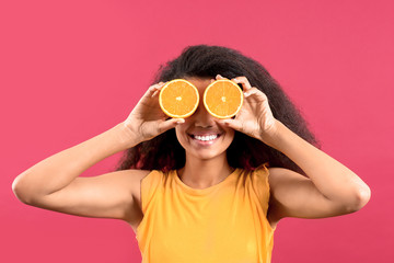 Happy African-American woman with orange fruit pieces on color background