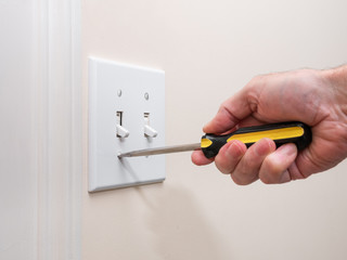 Male electrician repairing wall light switch panel. Handyman using screwdriver to install screw on light switch cover plate.