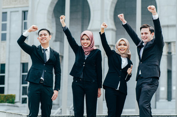 Group of young executive people in formalwear, arms raised to celebrate their success