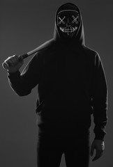 Anonymous criminal man with baseball bat in a black hoodie and neon mask