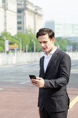 Portrait of young businessman Texting to Someone on his Mobile Phone with Happy Facial Expression.