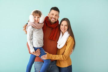 Happy family in winter clothes on color background