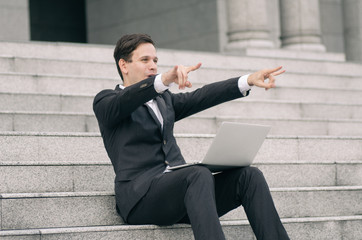 smiling and happy young business man sitting on stairs  working with his laptop