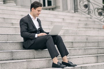 happy and motivated young business man sitting on stairs while working with his laptop