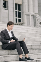 young handsome businessman with laptop relaxing on stairs, focus on laptop with smile face
