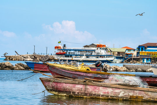 Colorful old wooden fishing boats docked and rope tied on the sea by the pier with birds on top in Montego Bay, Jamaica. Fishing is a traditional profession/ work/ job in tropical Caribbean islands.