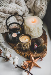 Christmas festive holiday mood composition with coffee in rustic cup, candles and decorative toys on wooden board, white woolen blanket at background, top view. Christmas greeting card