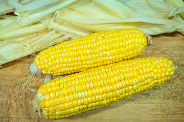 Patch of corn peeled on a wooden board on a background of leaves. Two pieces