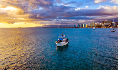 Fishing boat at sunset in Hawaii paradise with perfect clouds and orange and blue reflections in ocean