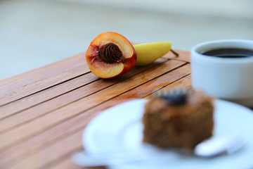 Half a peach and pears on a table. Fruit, a cup of coffee and a piece of chocolate cake on a wooden table. Horizontal, close-up, nobody.