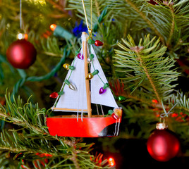 Red sailboat ornament hanging on a Christmas tree.  Closeup. 