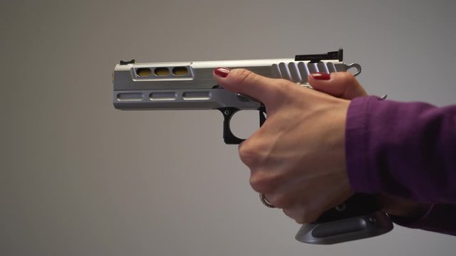 Close up of female with painted red nails, cocking and pulling trigger on large silver handgun