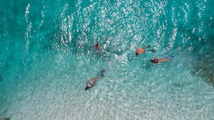 Foto op Canvas Young girls snorkeling in blue clear waters above coral reef on red sea in los roques venezuela . Travel and lifestyle concept. Top view. Three snorkelers swim in turquoise water © GARSPHOTO