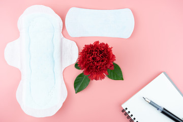 Red flowers with sanitary napkin and pen on notebook for note