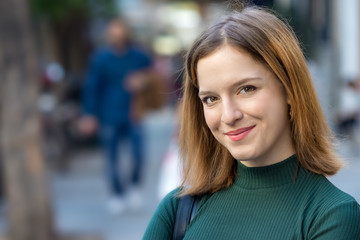 Portrait of a teenage woman looking camera with soft smile outdoors.