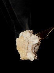 A piece of cooked chicken meat on a fork, steam smoke, black background.