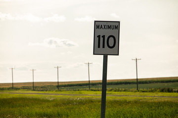 Selective focus view of 110 maximum speed limit sign on the roadside, against prairies and plains views on the Canadian rural country roads